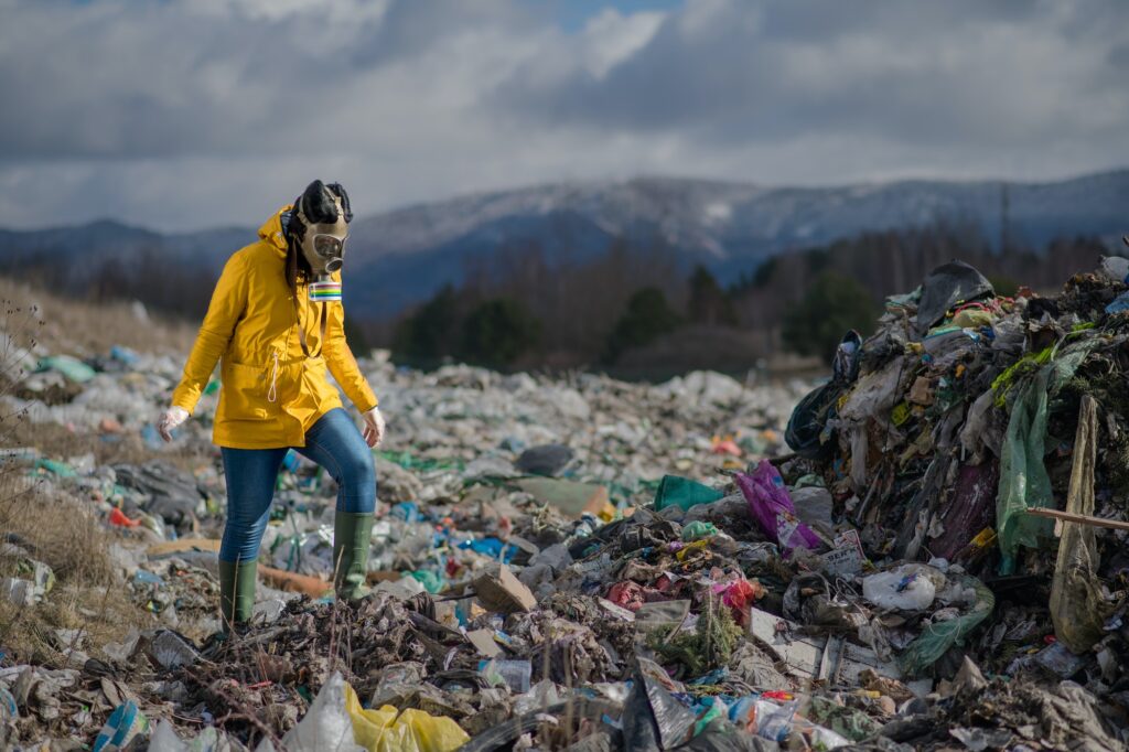 Woman with gas mask walking on landfill, environmental concept